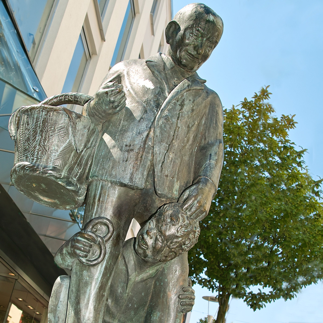 Ein kleiner Junge mit einer Brezel in der Hand schaut durch die Beine des Brezeladam - Bronzefigur  © Stadt Kaiserslautern