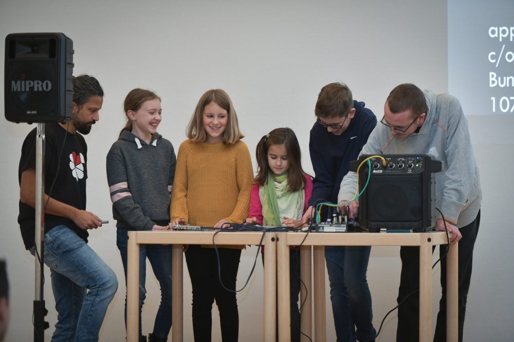Zwei Betreuer stehen mit Kindern auf einer Bühne und machen elektronische Musik.